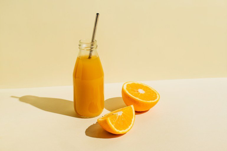 Colorful bottle of freshly pressed orange juice with fresh orange ingredients on beige background. Supervisors, healthy foods, drinks, diet and concept of detoxification. Lay flat, top view, copy space