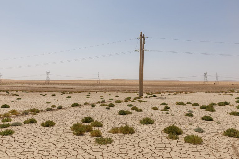 Sterile terrain in Afghanistan with cracked land, sparse vegetation and utility posts extending to the arid landscape.